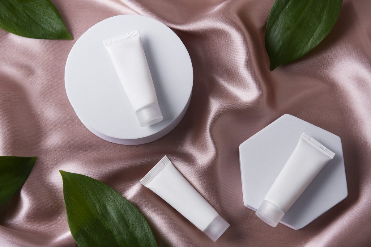 Eco-friendly cosmetic packaging tubes on satin, minimalist layout with natural leaves