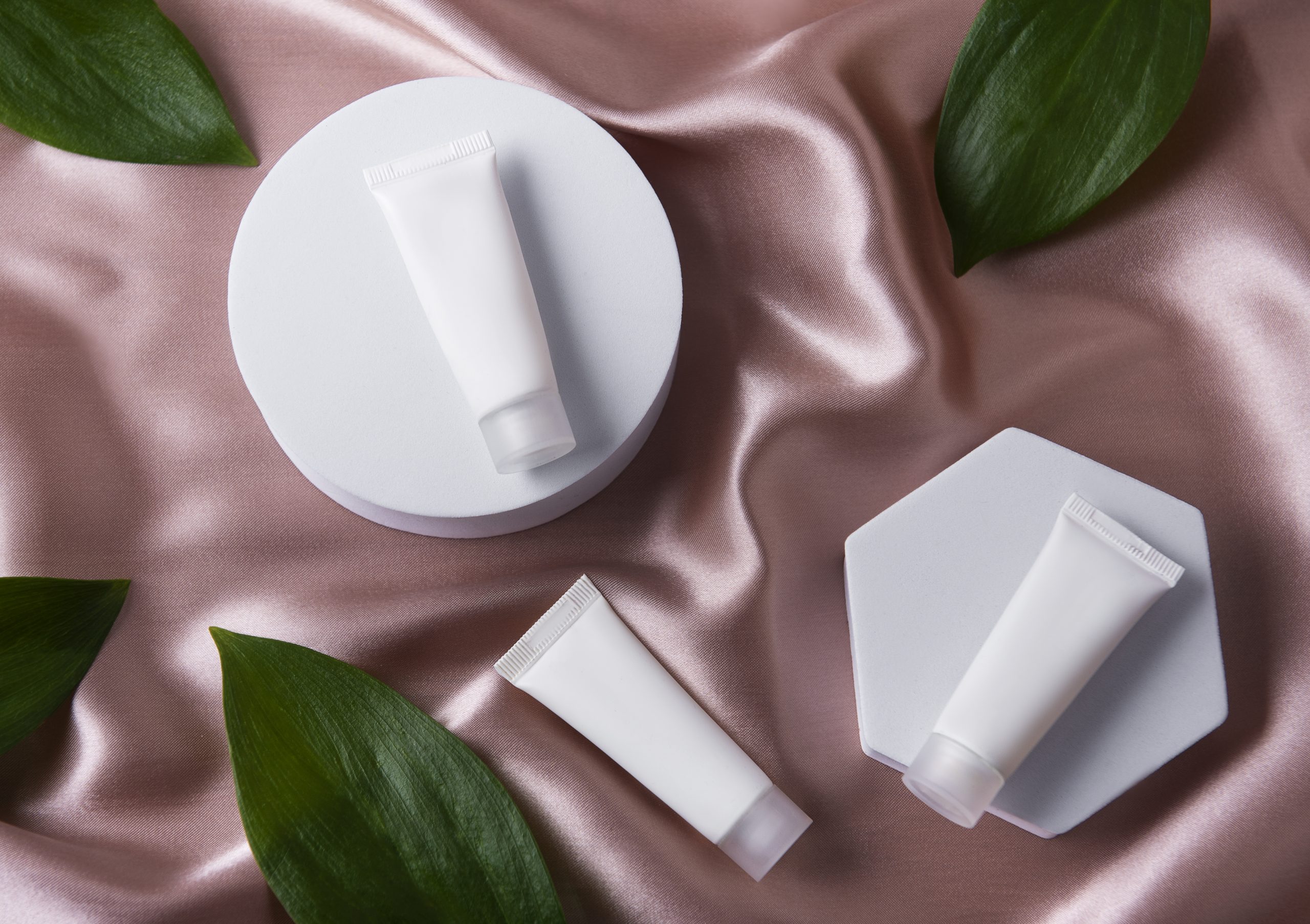 Eco-friendly cosmetic packaging tubes on satin, minimalist layout with natural leaves